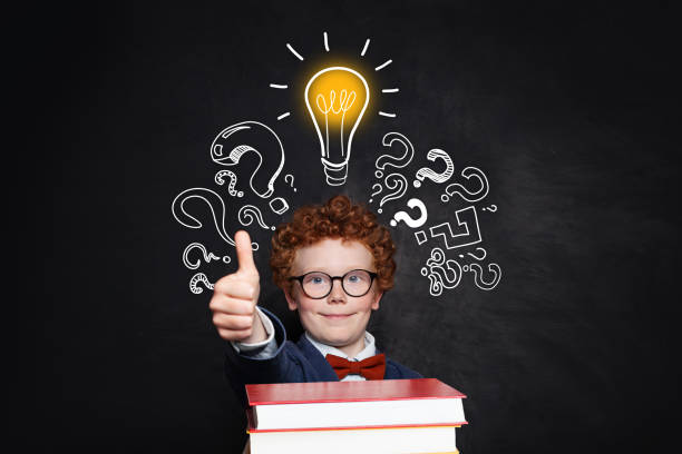istock Smart kid holding book and showing thumb up against lightbulb on chalkboard background. Brainstorming and idea concept 1158609942