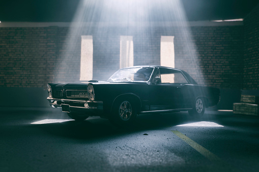 Beaconsfield, UK - June 26, 2019: A scale model of a Pontiac GTO in an old garage setting. The model car is sitting in an atmospherically-lit industrial garage environment. The garage environment/model is made out of fibre-board, and was photographed in my studio in Beaconsfield. There is no one in the photograph.