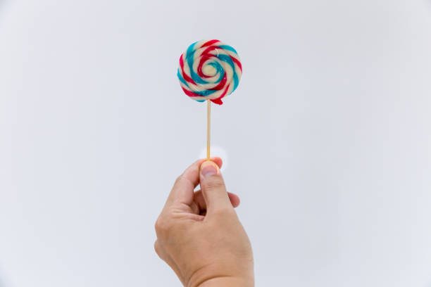 istock Fun and celebration concept.hand holding big colorful lollipop candy on stick, isolated on white background minimalism style. 1158611949