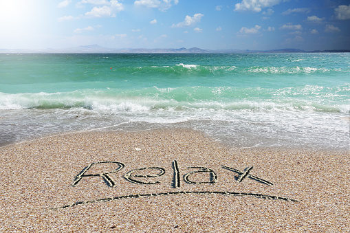 Relax word handwritten on beach sand with white feather on summer time