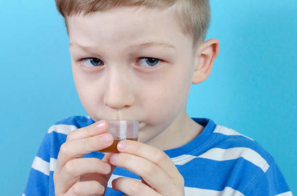 boy takes medicine syrup on blue background boy takes medicine syrup on blue background, closeup child liquid medicine stock pictures, royalty-free photos & images