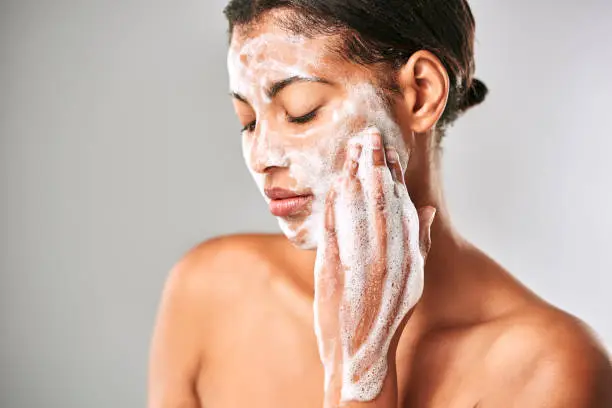 Cropped shot of a beautiful young woman washing her face against a grey background