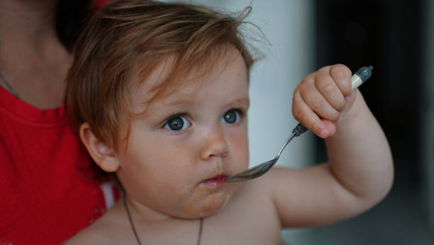 istock Adorable baby with spoon in mouth looking at camera 1158617022