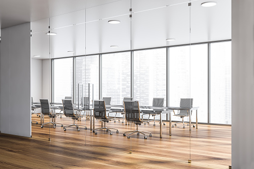 Corner of panoramic conference room with cityscape, wooden floor and glass meeting table with metal chairs as seen from office lobby. 3d rendering