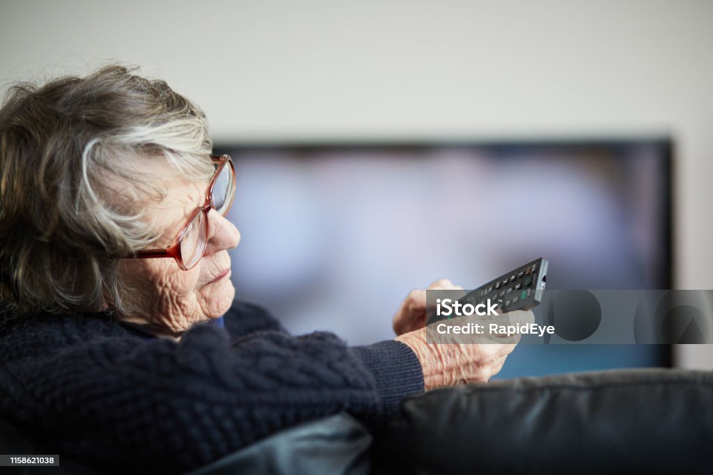 Senior woman irritated by her TV remote control Senior woman struggles with her remote. Watching TV Stock Photo