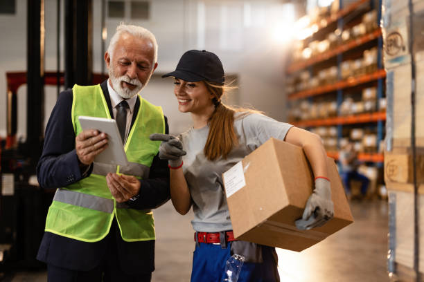 feliz hombre de negocios maduro y trabajadora femenina usando tableta digital en el compartimento de almacenamiento industrial. - compartimento para almacenamiento fotografías e imágenes de stock