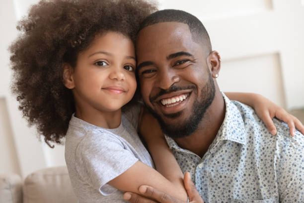 Happy african daddy and small cute child daughter embracing, portrait Happy affectionate african american family young daddy and small cute child daughter portrait, loving black dad and little mixed race kid girl bonding embrace looking at camera on fathers day concept happy fathers day funny stock pictures, royalty-free photos & images