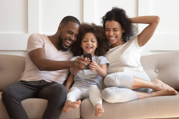 istock African daughter and parents looking at smartphone laughing on sofa 1158625016