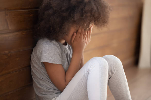 Upset african american child girl crying sitting alone on floor Upset small african american child girl crying covering face with hands sitting alone on floor, sad lonely orphan kid being bullied abused feeling stressed or scared, children violence abuse concept child abuse photos stock pictures, royalty-free photos & images