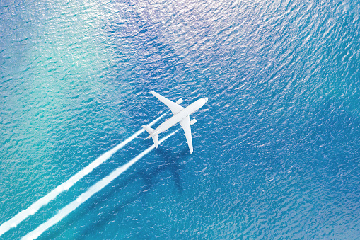 The plane flying over the sea leaves a white trail of smoke, a shadow on the surface of the water