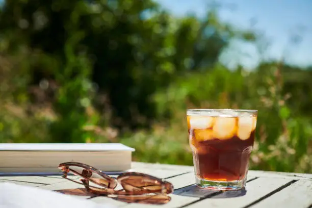 Photo of Summer Garden scene, Glass of black Iced Coffee on a garden table in bright sunshine.