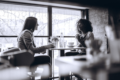 Two young multi-ethnic women drinking coffee in cafe.