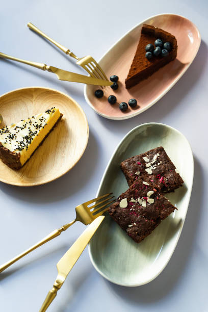 slices of cake desserts with berries and nuts on plates with different colors, pink, green, wooden material. golden fork with a knife for eating. chocolates, brownies, cheesecake. - cheesecake syrup almond cream imagens e fotografias de stock