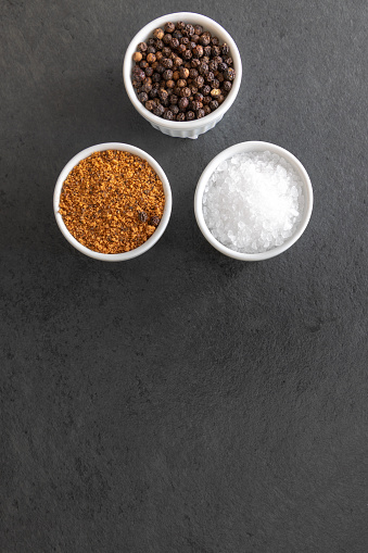 Sea salt, pepper grains and bbq rub on dark stone surface, close up with copy space