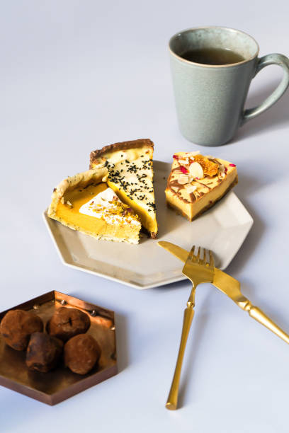 three slices of very sweet and tasty cheesecake on a plate with a geometric modern design in gray. golden fork with a knife for eating. chocolate black candy. a cup of tea or coffee. sugar addiction. - cheesecake syrup almond cream imagens e fotografias de stock