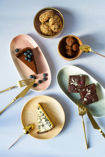 slices of cake desserts with berries and nuts on plates with different colors, pink, green, wooden material. golden fork with a knife for eating. tea spoon. chocolates, brownies, cheesecake, biscuits. - cheesecake syrup almond cream imagens e fotografias de stock