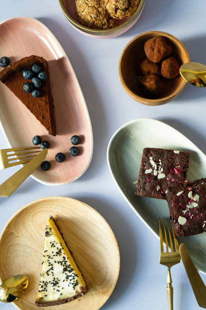 slices of cake desserts with berries and nuts on plates with different colors, pink, green, wooden material. golden fork with a knife for eating. tea spoon. chocolates, brownies, cheesecake, biscuits. - cheesecake syrup almond cream imagens e fotografias de stock