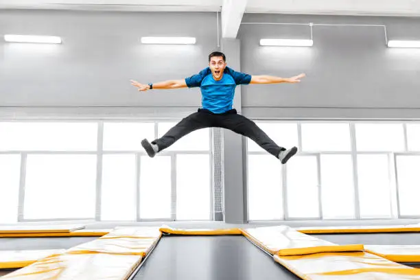 A young fit happy man jumping and flying on trampoline in fitness gym