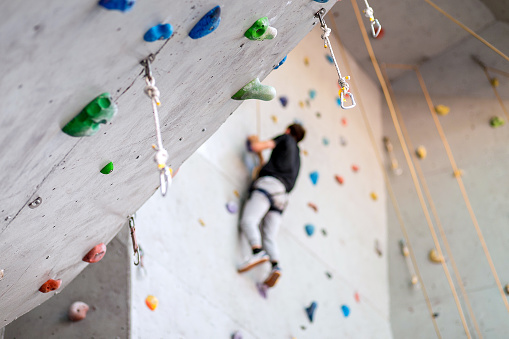 hombre escalando en la pared práctica interior, asegurando mosquetones y cuerda photo
