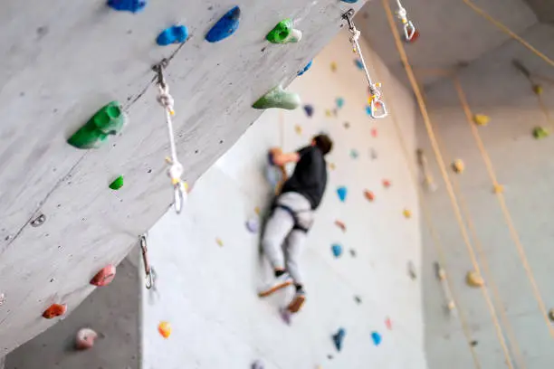 Photo of man climbing on practical wall indoor, securing carabiners and rope