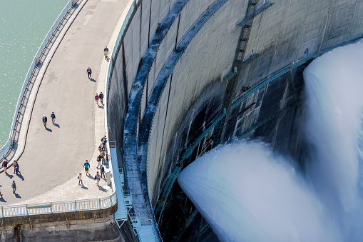 Closeup View Of Water Turbines Are Producing Electricity At Power Plant. Panorama View Of Hydro Power Station And People On The Kurobe Lake Dam,Toyama. River Dam and Tateyama Mountains.