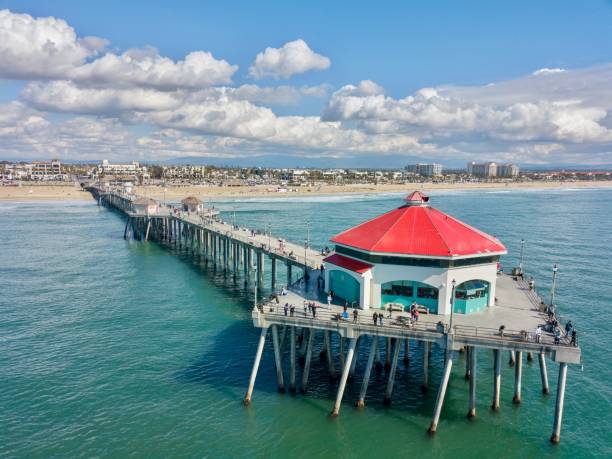 Drone view of the Huntington Beach Pier in Huntington Beach, Orange County, California Aerial drone view of the Huntington Beach Pier against blue sky with clouds huntington beach california stock pictures, royalty-free photos & images