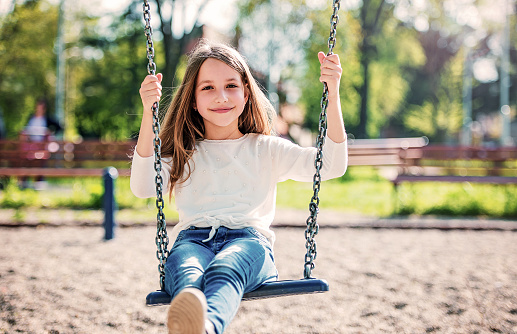 Children playground. Cute little girl having fun with a swing in the park