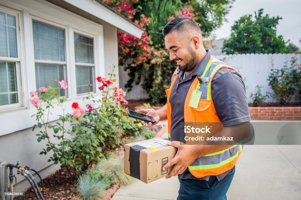 Young Male Hispanic Delivery Man Takes Package to Home A young hispanic man delivering packages in a residential neighborhood. Delivering Stock Photo