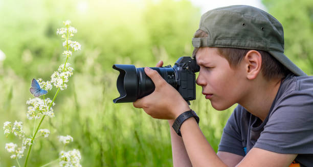 menino que prende a câmera digital e a borboleta do tiro na flor selvagem - aprender fotos - fotografias e filmes do acervo