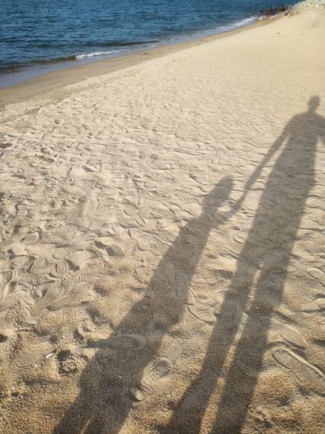 istock Sunset walking by the beach shadow with a kids holding hand on sand 1158674491