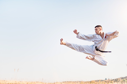 Young martial artist practicing flying kicks in nature.