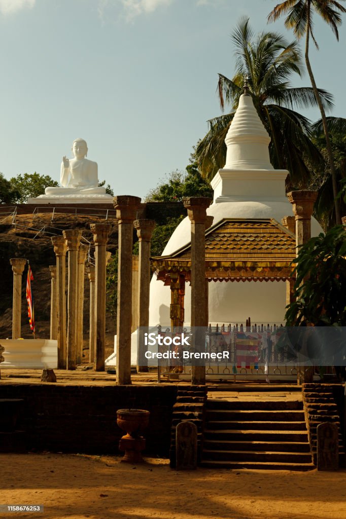 Ambasthala Dagoba and Buddha Statue in Mihintale Ambasthala Dagoba, a small stupa surrounded with stone pillars, with big Buddha Statue in Mihintale, Sri Lanka. Architectural Column Stock Photo