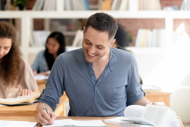 lächelnde männliche student in der bibliothek vorbereitung für test - male education college student nerd stock-fotos und bilder