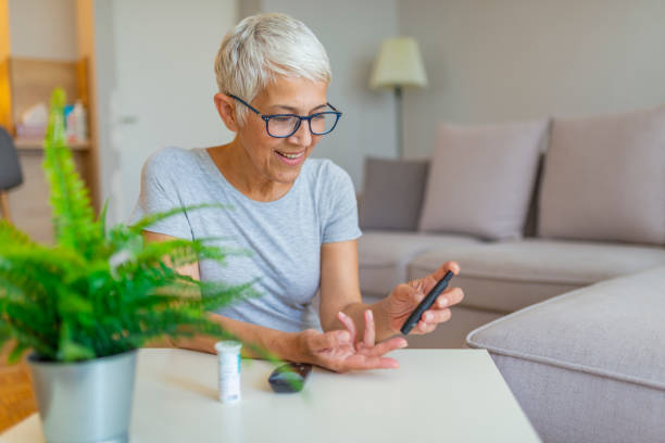 happy mature woman with glucometer checking blood sugar level at home - diabetes blood sugar test insulin glucose imagens e fotografias de stock