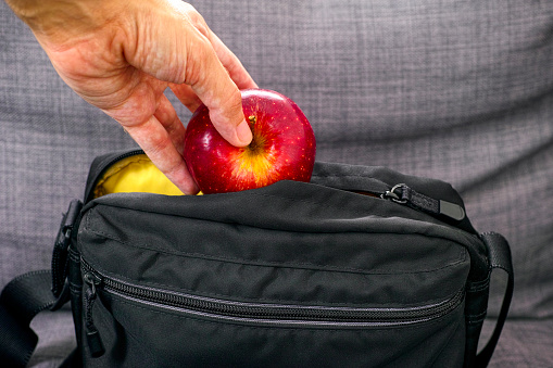 Person hand taking red apple from black bag. Close up.