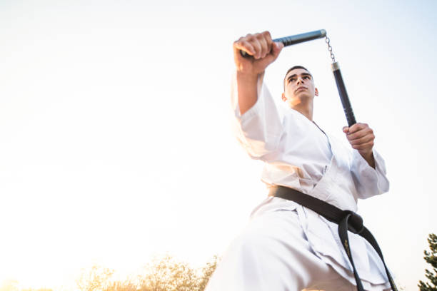 vue d'angle bas de jeune artiste martial utilisant l'arme de nunchaku. - nunchaku photos et images de collection