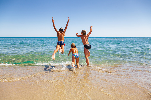 Happy children having fun on a beach running and jumping to the sea enjoying summer vacation