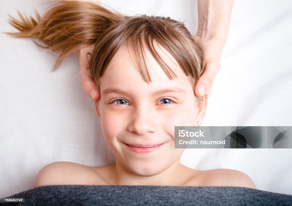 Girl receiving osteopathic treatment of her head in pediatric clinic Elementary age girl's head being manipulated by osteopathic or chiropractic manual therapist in a pediatric clinic Osteopath Stock Photo