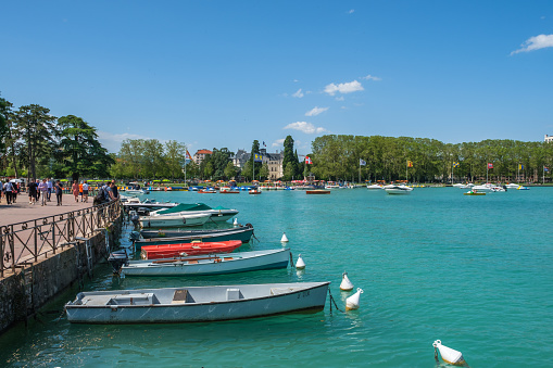 Tourists in a park on a beautiful sunny day along the quay with  boats in the blue water of Lake Annecy, France