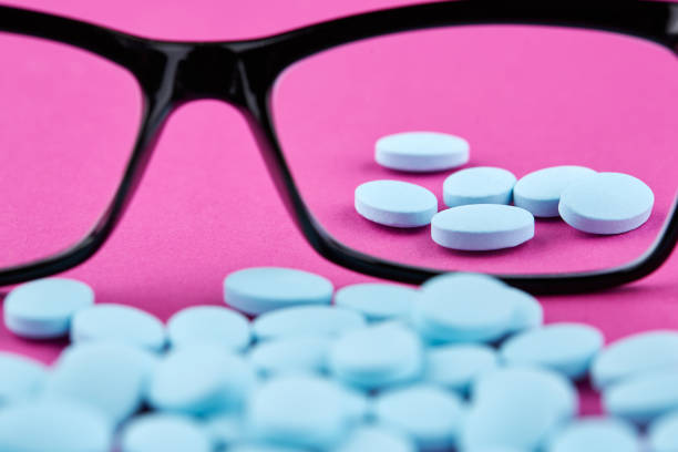 istock Glasses and blue pills on pink background. Medicine 1158686584