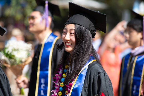 Students Walk in Graduation Procession Wearing Cap and Gown One asian female student stands out from the crowd of graduating college students at UCLA. ucla photos stock pictures, royalty-free photos & images