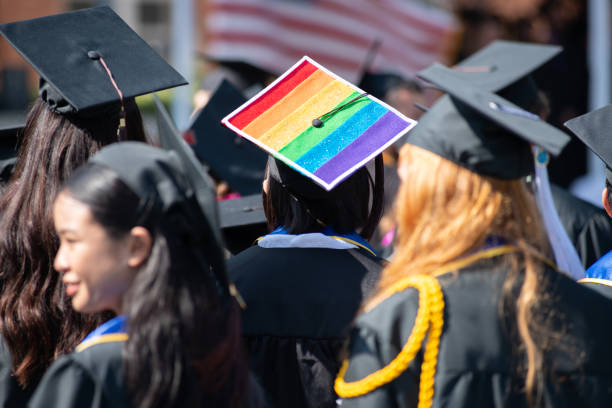 Woman Wears Graduation Cap and Gown Showing Gay Pride One student stands out from the rest of the graduation crowd in their solid black cap and gowns except for one brave lesbian woman who wears her gay pride colors proudly on her cap. ucla photos stock pictures, royalty-free photos & images