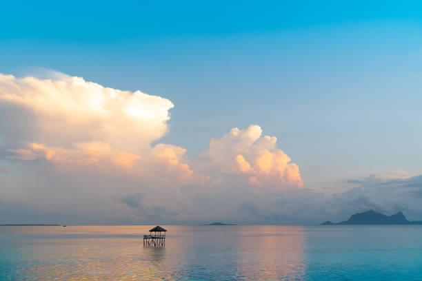Rising sun highlights gathering clouds above sea with single fisherman's platform