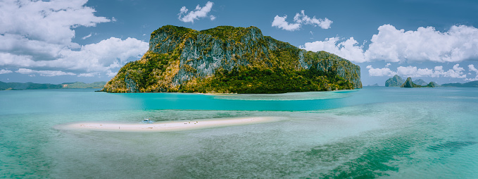 Palawan, Philippines. Aerial drone panoramic view of sandbar with lonely tourist boat in turquoise coastal shallow waters and coral reef in El Nido archipelago.