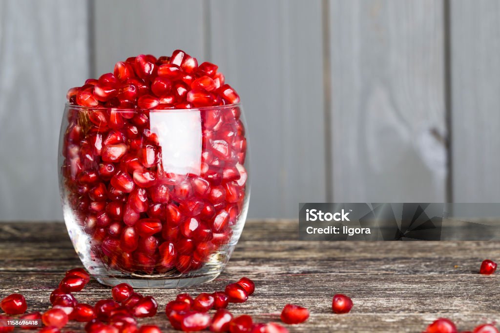 ripe pomegranate tasty sweet grains of ripe pomegranate on a wooden table, close-up of wholesome berries while breaking a whole fruit , small grains in a transparent glass cup Acid Stock Photo