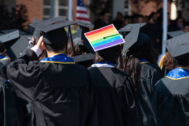 Woman Wears Graduation Cap and Gown Showing Gay Pride One student stands out from the rest of the graduation crowd in their solid black cap and gowns except for one brave lesbian woman who wears her gay pride colors proudly on her cap. ucla photos stock pictures, royalty-free photos & images
