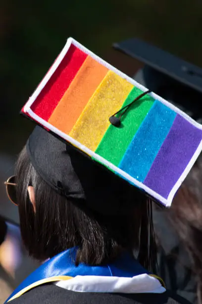 One student stands out from the rest of the graduation crowd in their solid black cap and gowns except for one brave lesbian woman who wears her gay pride colors proudly on her cap.
