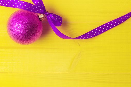 Pink Christmas ball with long ribbon on yellow background
