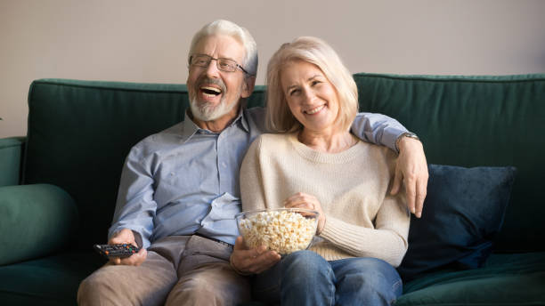 istock Laughing mature spouses sitting on couch watching comedy at home 1158702059