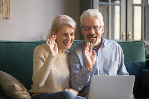 Aged couple looks at computer screen wave hands greeting friend